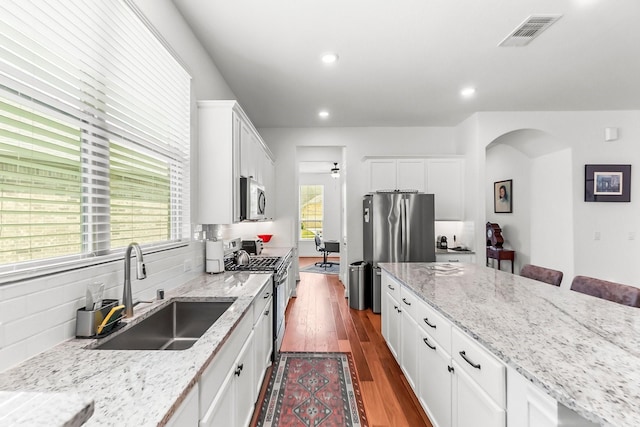 kitchen featuring stainless steel appliances, light stone counters, white cabinetry, and sink