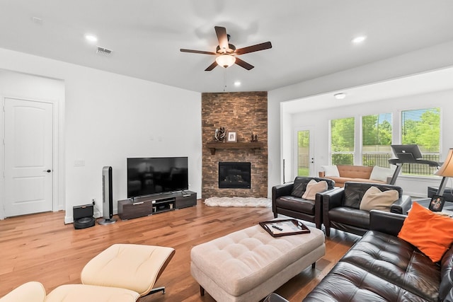 living room with hardwood / wood-style flooring, ceiling fan, and a stone fireplace