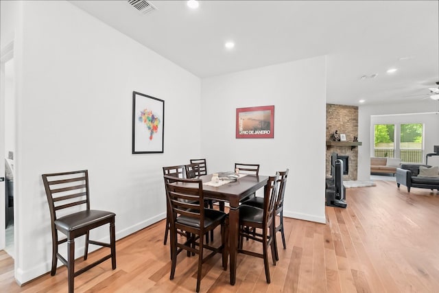 dining room featuring light wood-type flooring, a stone fireplace, and ceiling fan