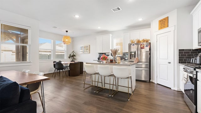 kitchen with white cabinetry, decorative light fixtures, decorative backsplash, a kitchen island, and appliances with stainless steel finishes