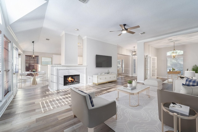 living room with crown molding, vaulted ceiling, a tiled fireplace, ceiling fan with notable chandelier, and hardwood / wood-style flooring