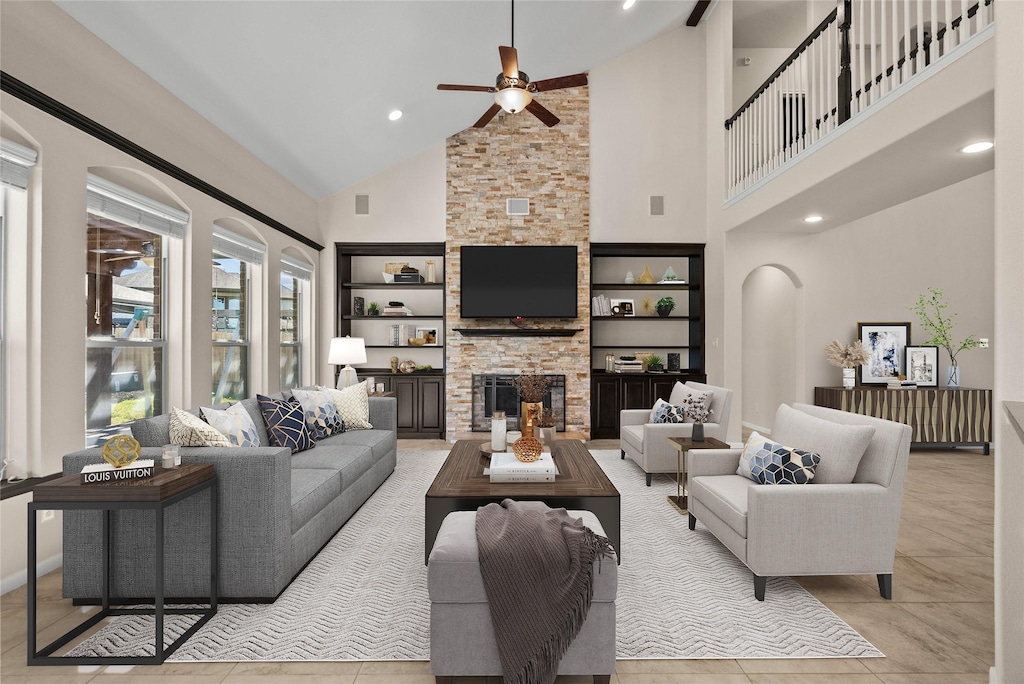 living room featuring ceiling fan, a stone fireplace, high vaulted ceiling, and built in shelves