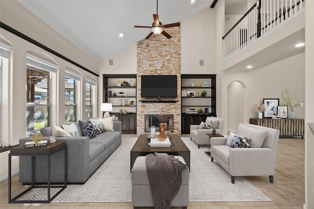 tiled living room with a high ceiling, a stone fireplace, ceiling fan, and built in shelves