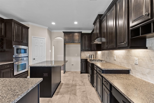 kitchen featuring tasteful backsplash, light stone counters, dark brown cabinetry, stainless steel appliances, and crown molding