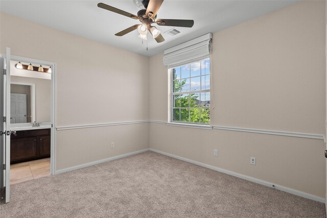 unfurnished bedroom featuring ceiling fan, light colored carpet, sink, and ensuite bath