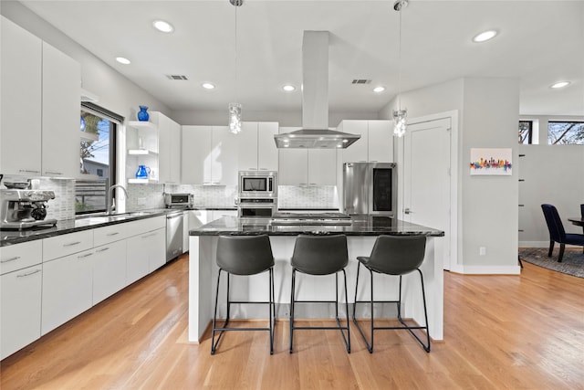 kitchen with island exhaust hood, appliances with stainless steel finishes, hanging light fixtures, a kitchen island, and white cabinets