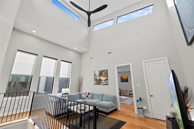 living room featuring light hardwood / wood-style floors, a high ceiling, and ceiling fan