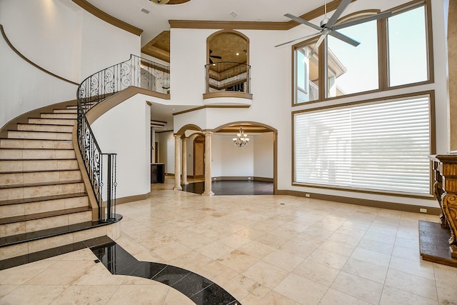 entrance foyer with ceiling fan with notable chandelier, ornate columns, crown molding, and a high ceiling