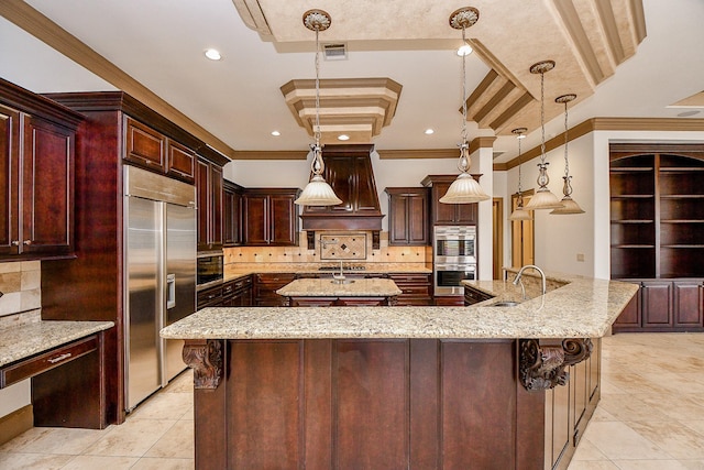 kitchen featuring a large island with sink, a raised ceiling, ornamental molding, appliances with stainless steel finishes, and decorative light fixtures