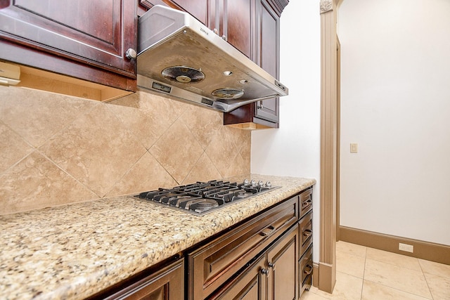 kitchen featuring light stone countertops, stainless steel gas cooktop, backsplash, extractor fan, and light tile patterned floors