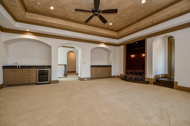 unfurnished living room with light colored carpet, a raised ceiling, beverage cooler, and ceiling fan