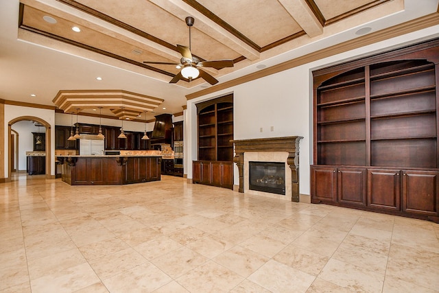 unfurnished living room with built in shelves, ceiling fan, beamed ceiling, a fireplace, and ornamental molding