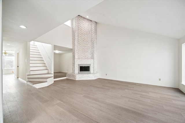 unfurnished living room featuring ceiling fan, a fireplace, lofted ceiling, and light wood-type flooring