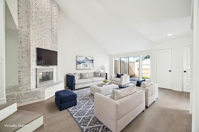 living room with light hardwood / wood-style flooring, high vaulted ceiling, and a brick fireplace