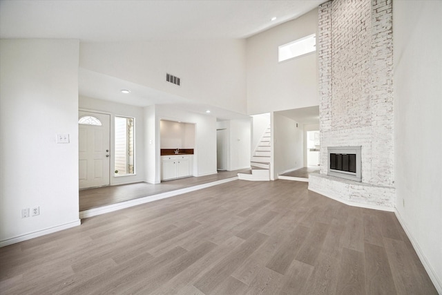 unfurnished living room featuring hardwood / wood-style floors, a towering ceiling, and a brick fireplace