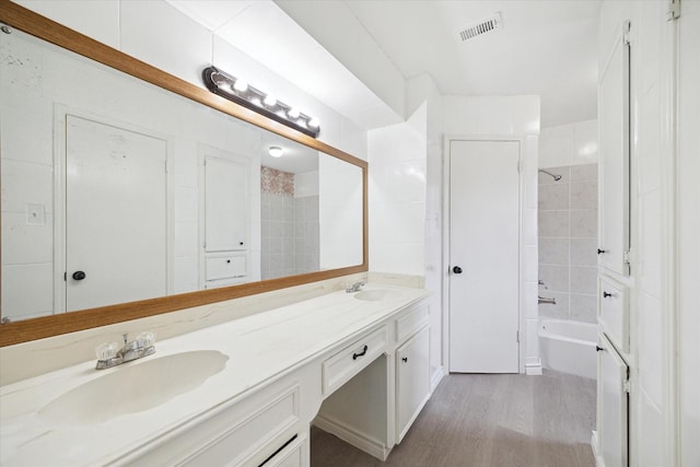 bathroom with hardwood / wood-style flooring, vanity, and tiled shower / bath