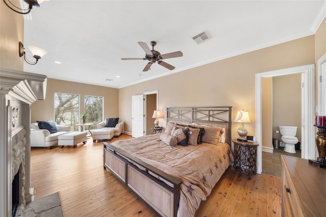 bedroom featuring ensuite bath, a fireplace, ceiling fan, and light wood-type flooring