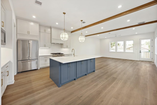 kitchen with decorative light fixtures, white cabinetry, an island with sink, stainless steel fridge, and decorative backsplash