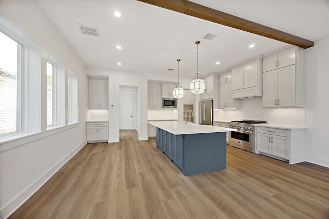 kitchen with beamed ceiling, tasteful backsplash, a center island with sink, high quality appliances, and pendant lighting