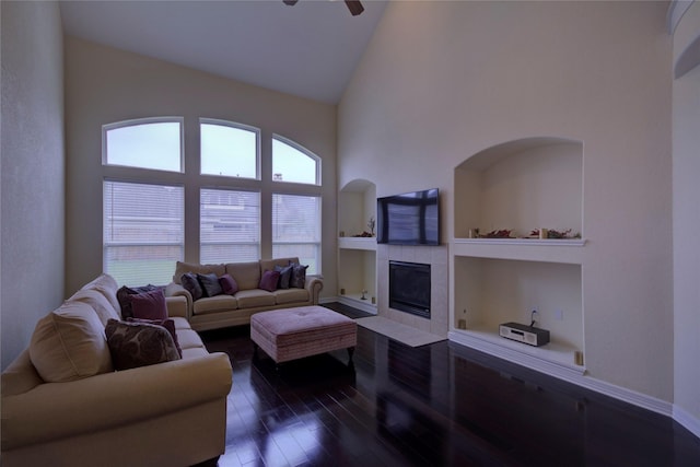 living room with a tile fireplace, ceiling fan, high vaulted ceiling, dark hardwood / wood-style floors, and built in shelves