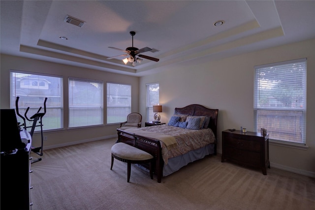 bedroom featuring ceiling fan, light carpet, and a tray ceiling