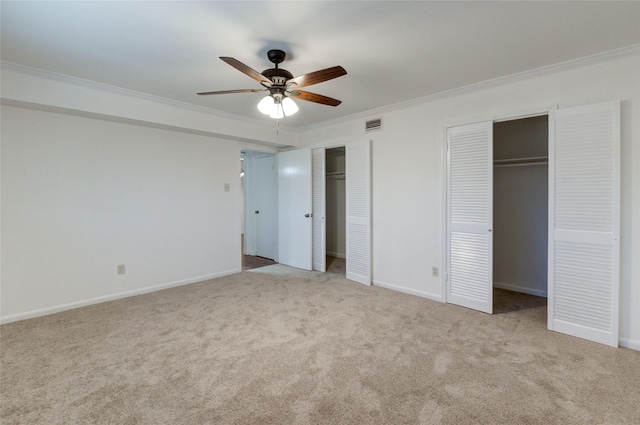 unfurnished bedroom with two closets, ceiling fan, crown molding, and light colored carpet