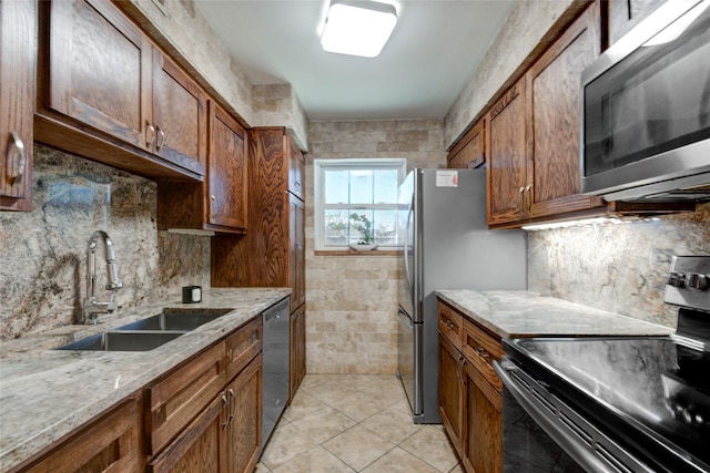 kitchen featuring light tile patterned floors, light stone counters, a sink, appliances with stainless steel finishes, and brown cabinetry