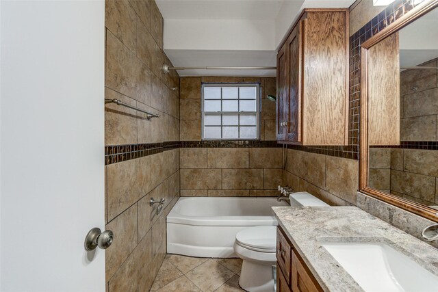 full bathroom with vanity, tile patterned floors, tiled shower / bath combo, toilet, and tile walls