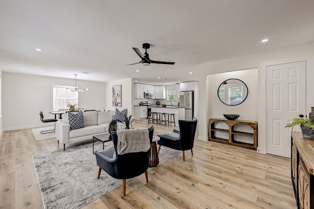 living room featuring ceiling fan with notable chandelier and light hardwood / wood-style flooring