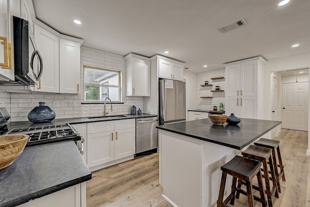 kitchen with white cabinets, stainless steel appliances, a kitchen island, and sink