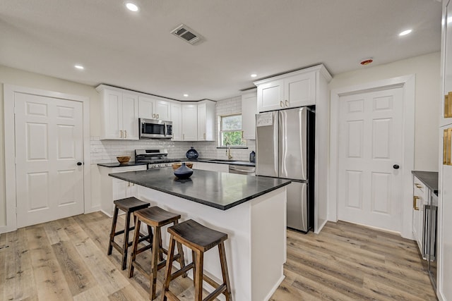 kitchen with light wood-type flooring, a breakfast bar, stainless steel appliances, white cabinets, and a kitchen island