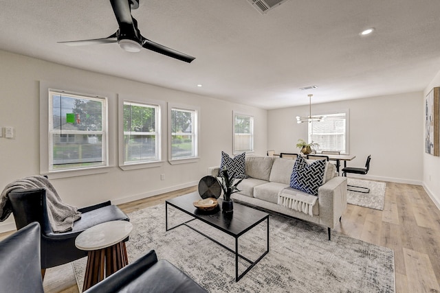 living room with ceiling fan with notable chandelier and light hardwood / wood-style flooring