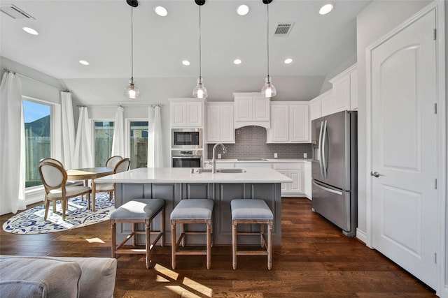 kitchen with sink, hanging light fixtures, stainless steel appliances, decorative backsplash, and a center island with sink