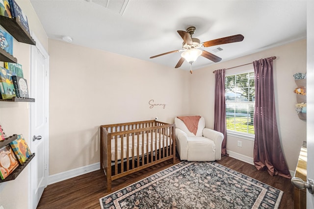 bedroom featuring ceiling fan, a crib, and dark wood-type flooring