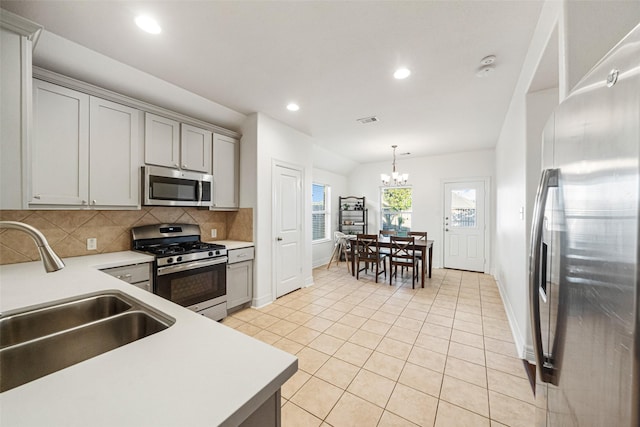 kitchen featuring backsplash, gray cabinetry, stainless steel appliances, sink, and a chandelier