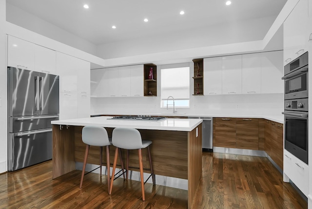 kitchen with a spacious island, a breakfast bar, appliances with stainless steel finishes, dark hardwood / wood-style floors, and white cabinets