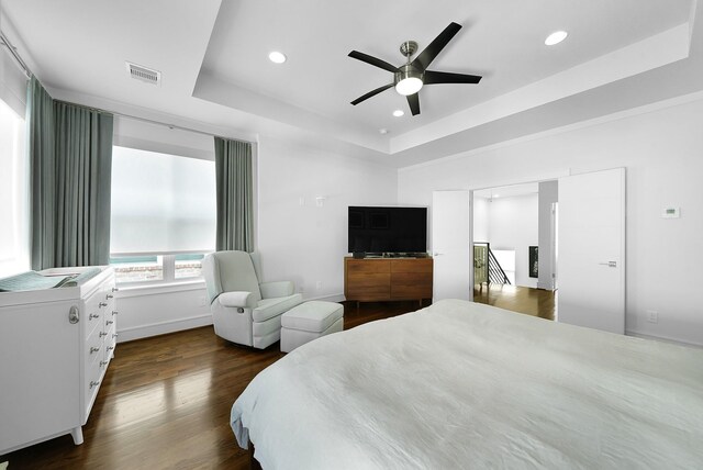 bedroom with dark hardwood / wood-style flooring, a tray ceiling, and ceiling fan