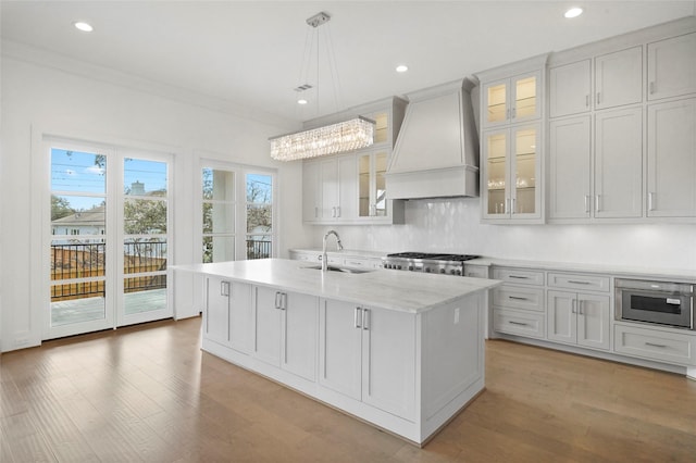 kitchen with custom range hood, sink, pendant lighting, white cabinets, and an island with sink