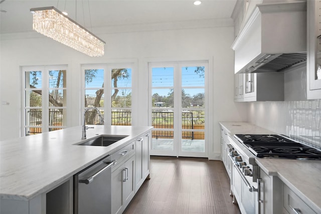 kitchen featuring an inviting chandelier, sink, wall chimney exhaust hood, an island with sink, and decorative light fixtures