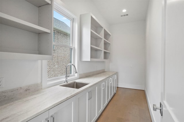 kitchen featuring white cabinets, light stone countertops, sink, and light hardwood / wood-style flooring