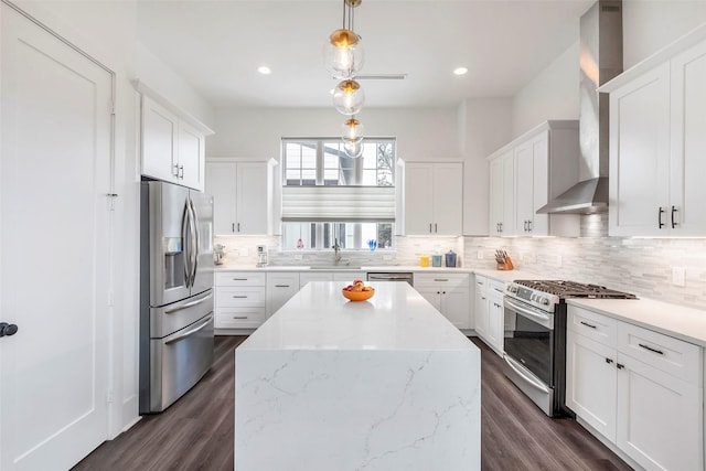 kitchen with white cabinets, wall chimney range hood, light stone countertops, decorative light fixtures, and stainless steel appliances