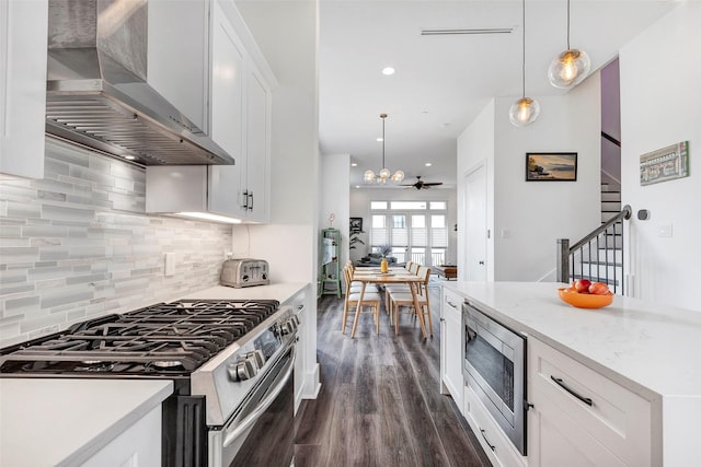 kitchen featuring white cabinetry, ceiling fan, wall chimney range hood, pendant lighting, and appliances with stainless steel finishes