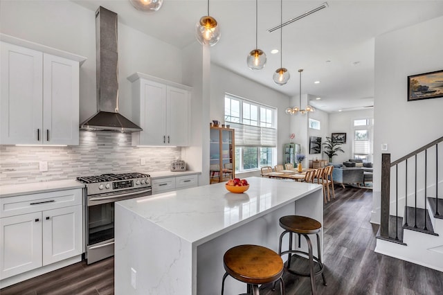 kitchen featuring gas stove, white cabinetry, a center island, wall chimney exhaust hood, and backsplash