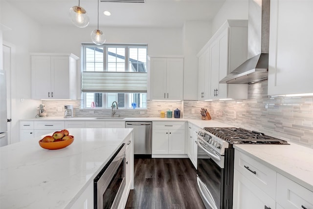 kitchen featuring pendant lighting, backsplash, wall chimney range hood, white cabinetry, and stainless steel appliances