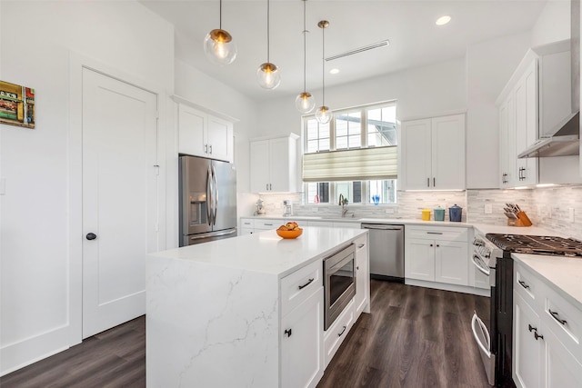 kitchen with a kitchen island, backsplash, decorative light fixtures, white cabinets, and appliances with stainless steel finishes