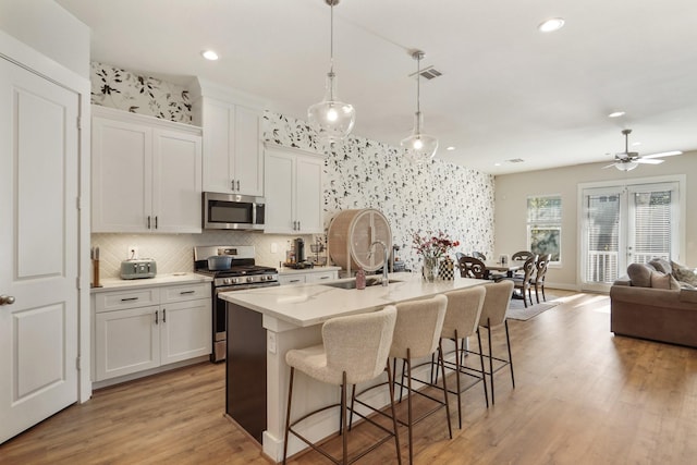 kitchen with stainless steel appliances, ceiling fan, white cabinets, hanging light fixtures, and an island with sink