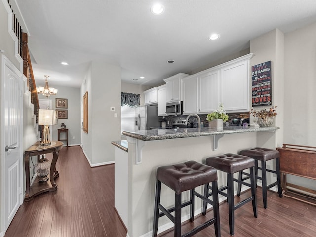 kitchen featuring kitchen peninsula, appliances with stainless steel finishes, tasteful backsplash, stone counters, and white cabinets