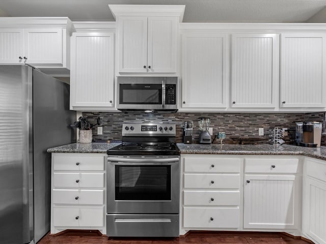 kitchen featuring appliances with stainless steel finishes, backsplash, white cabinetry, and dark stone countertops