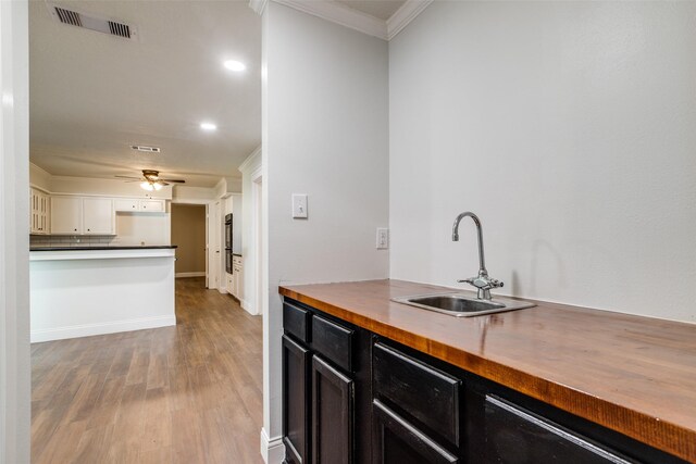 kitchen with sink, wood counters, light hardwood / wood-style flooring, crown molding, and white cabinets