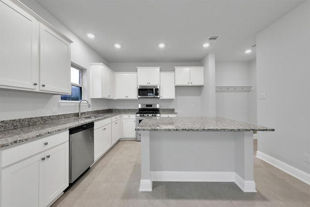 kitchen with sink, a kitchen island, light stone counters, white cabinetry, and stainless steel appliances